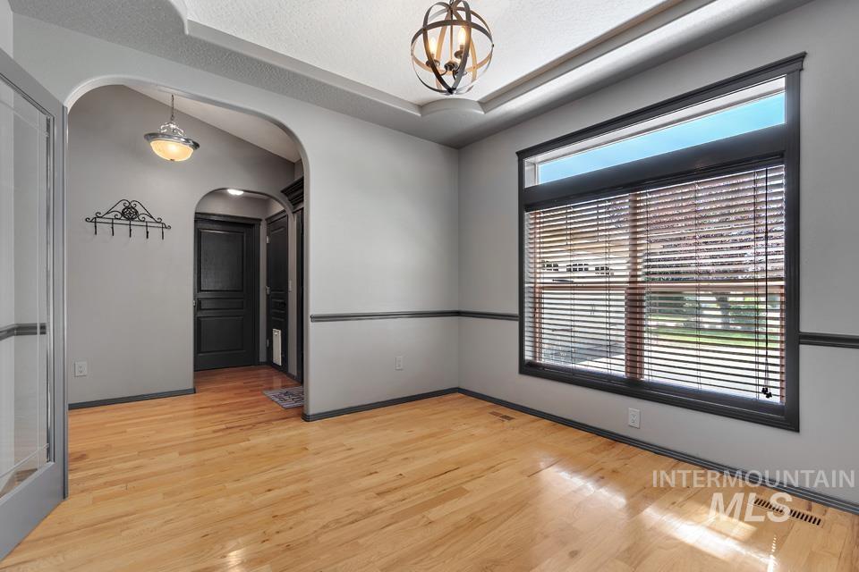 Empty room featuring light wood-style flooring, a raised ceiling, arched walkways, and a chandelier