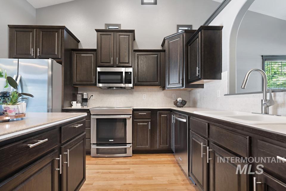 Kitchen featuring dark brown cabinets, appliances with stainless steel finishes, tasteful backsplash, and light wood-style floors