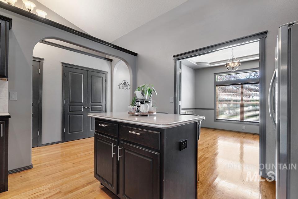 Kitchen featuring light wood finished floors, freestanding refrigerator, arched walkways, a kitchen island, and light stone countertops