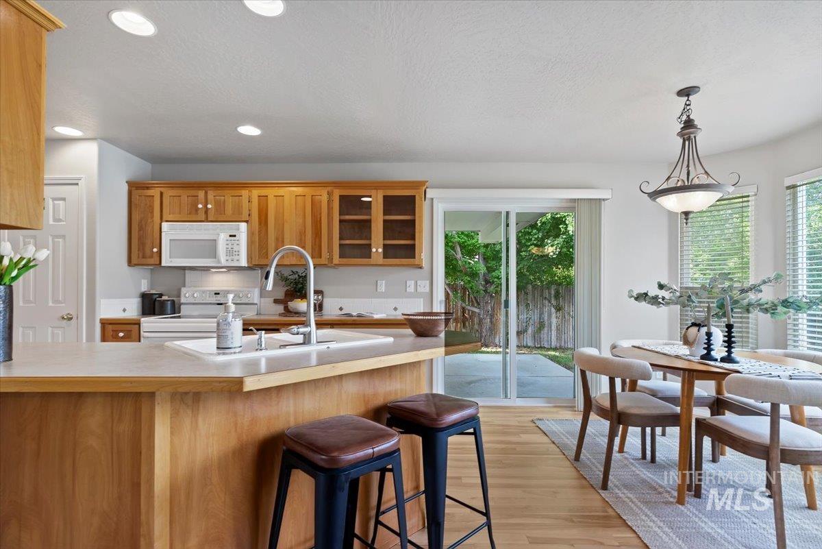 Kitchen with glass insert cabinets, brown cabinetry, light countertops, light wood-style flooring, and a kitchen bar