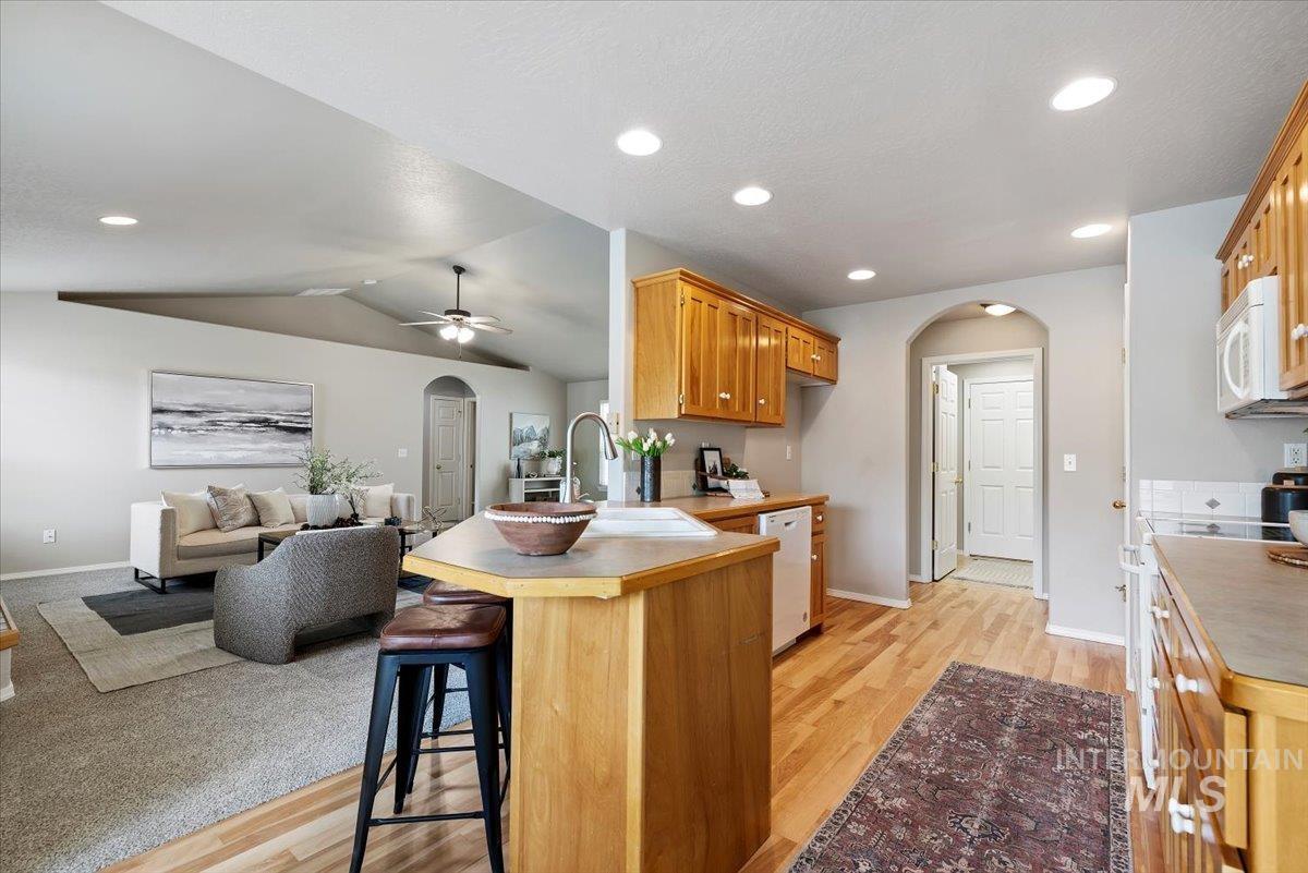 Kitchen with arched walkways, a peninsula, a breakfast bar, light wood-style floors, and lofted ceiling