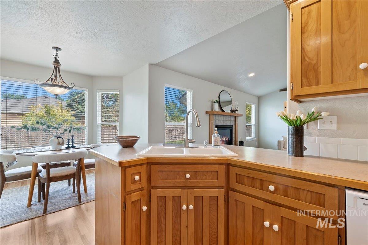 Kitchen with light countertops, light wood-style floors, hanging light fixtures, a tiled fireplace, and a peninsula
