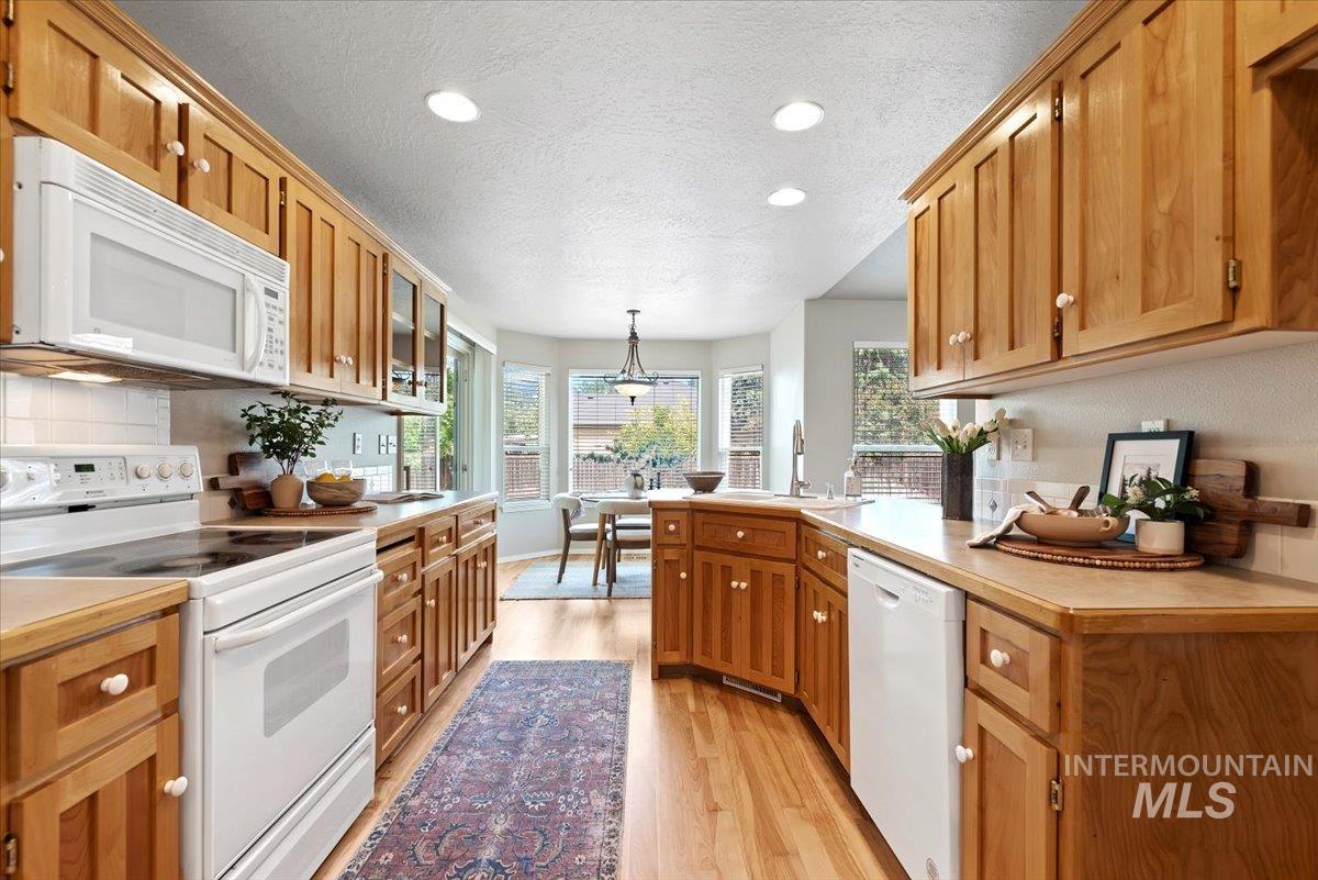 Kitchen with white appliances, light countertops, light wood-style floors, a textured ceiling, and brown cabinets