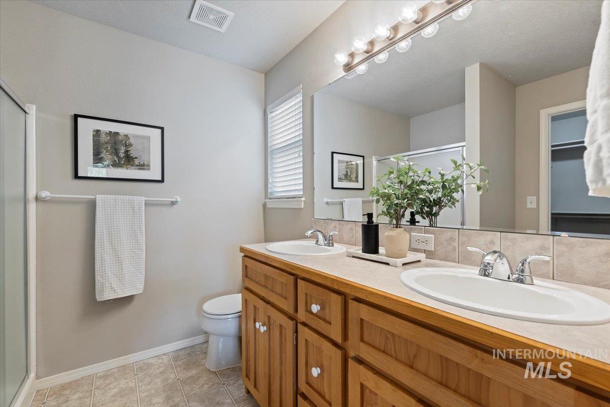 Bathroom featuring a shower stall, double vanity, light tile patterned floors, and tasteful backsplash
