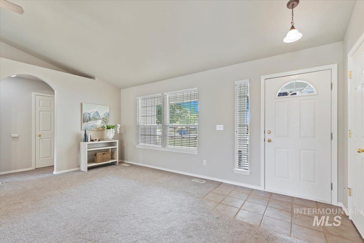 Entrance foyer with light colored carpet, vaulted ceiling, light tile patterned floors, and arched walkways