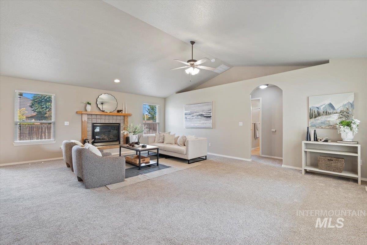 Living room featuring arched walkways, lofted ceiling, a fireplace, light carpet, and ceiling fan