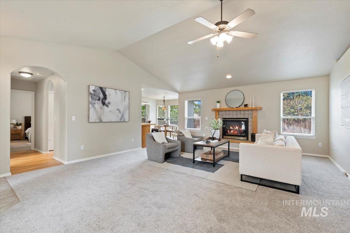Living area with plenty of natural light, light colored carpet, lofted ceiling, a tiled fireplace, and arched walkways