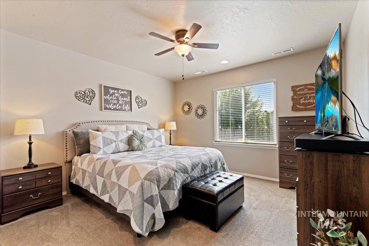 Bedroom with light carpet, ceiling fan, and a textured ceiling
