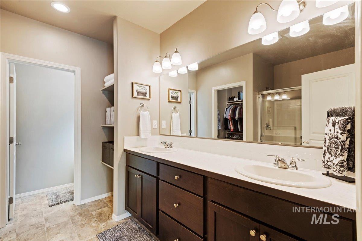 Bathroom featuring a shower stall, a walk in closet, double vanity, and recessed lighting