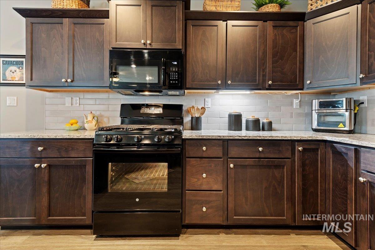 Kitchen featuring black appliances, tasteful backsplash, dark brown cabinets, and light stone counters