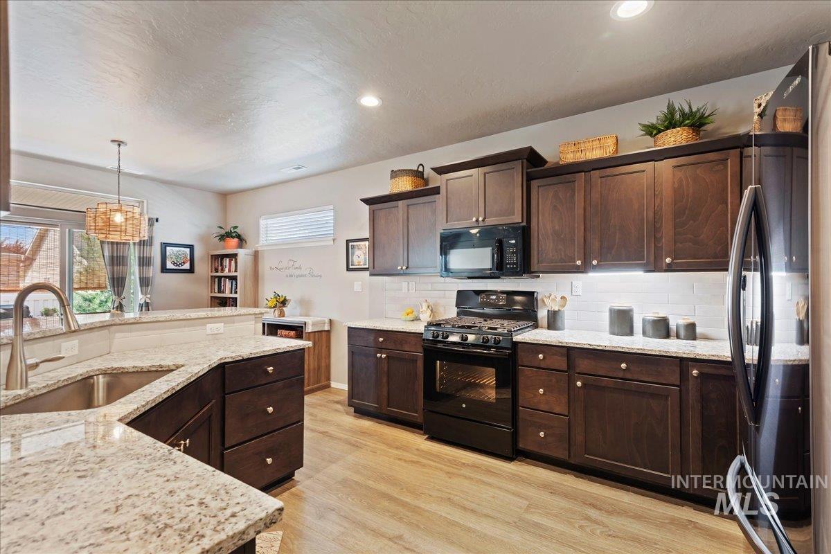 Kitchen with black appliances, tasteful backsplash, dark brown cabinetry, light wood-style floors, and hanging light fixtures