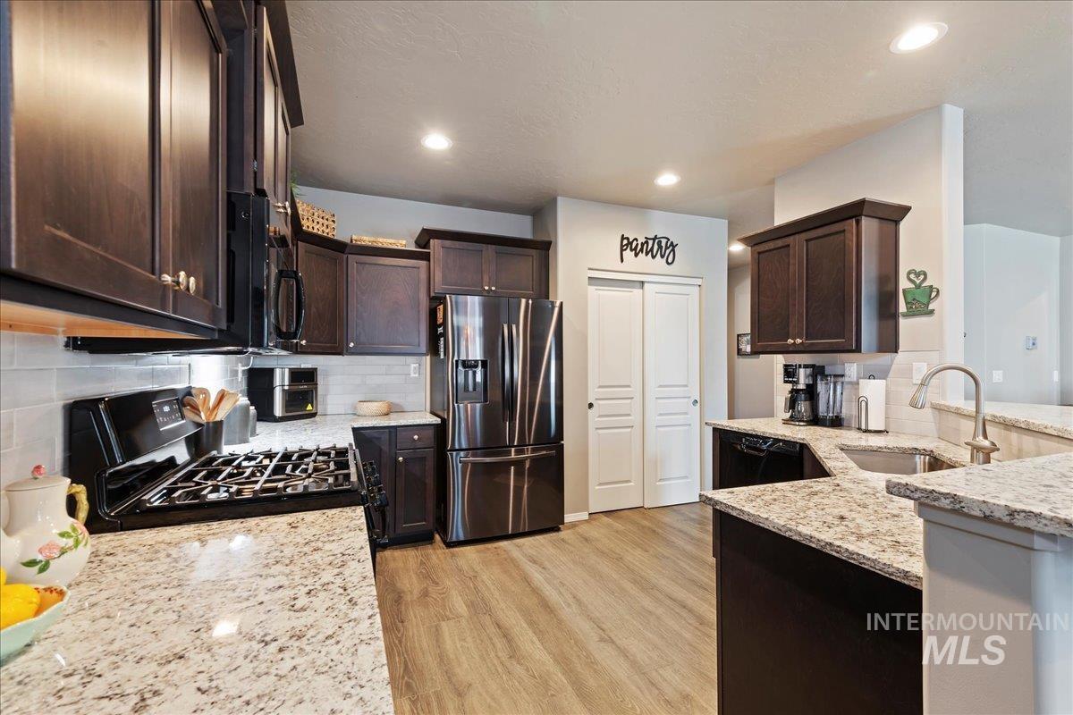 Kitchen with black appliances, dark brown cabinetry, light stone counters, and recessed lighting