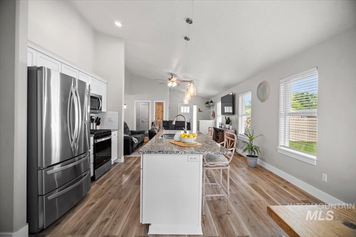 Kitchen featuring appliances with stainless steel finishes, light stone countertops, a breakfast bar, a center island with sink, and white cabinets