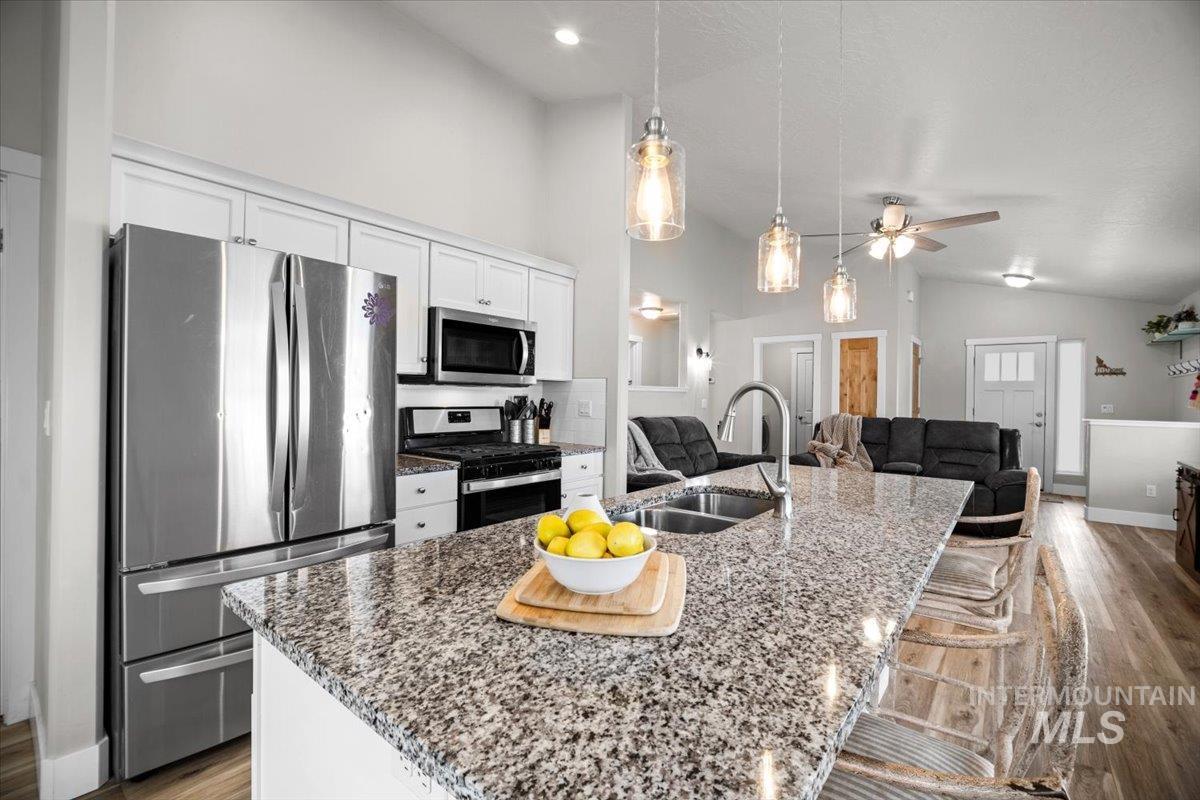 Kitchen with light wood-style floors, stainless steel appliances, dark stone countertops, a center island with sink, and ceiling fan