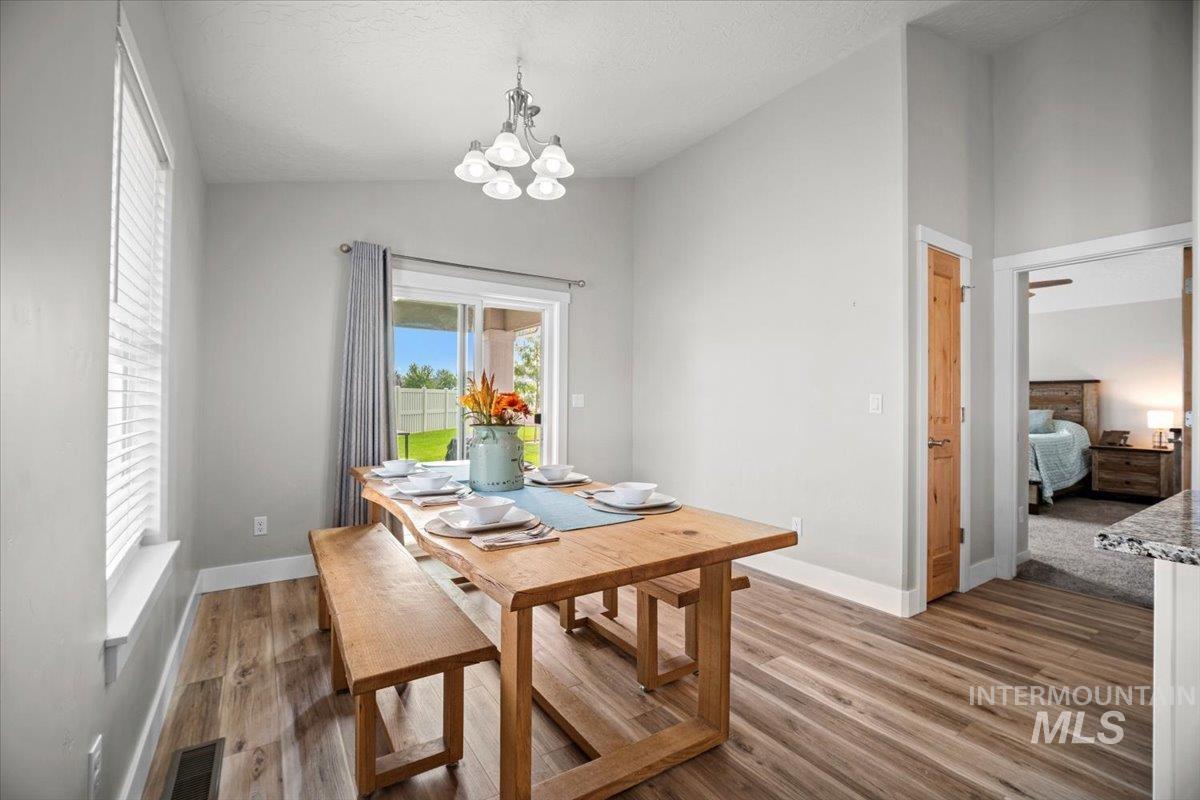 Dining space with vaulted ceiling, light wood finished floors, a chandelier, and a textured ceiling