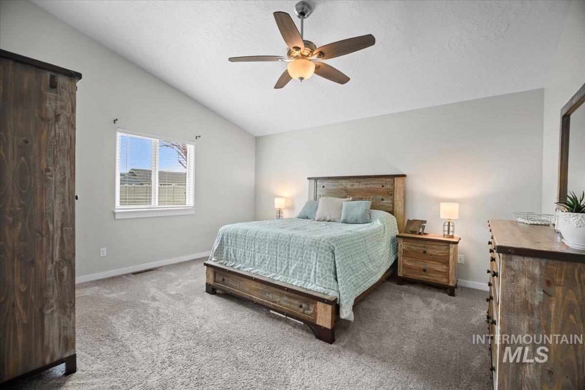 Carpeted bedroom featuring lofted ceiling, a ceiling fan, and a textured ceiling