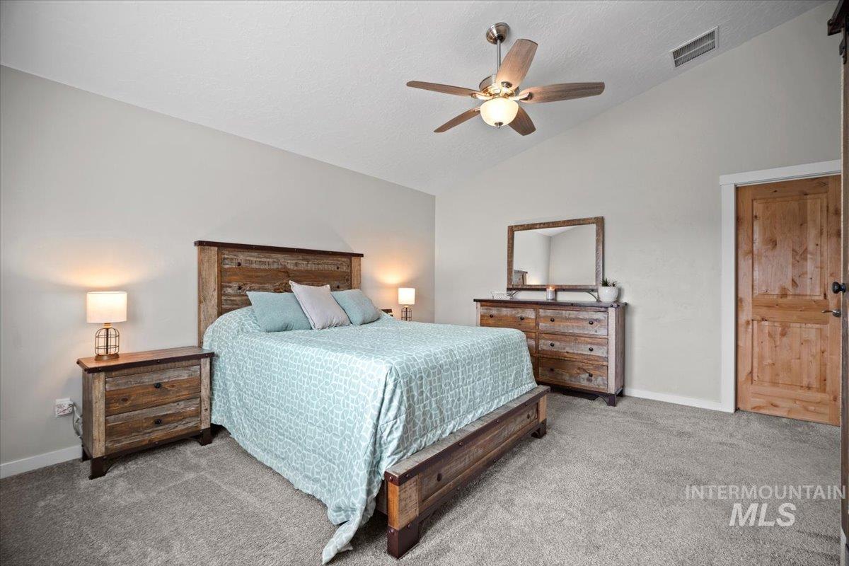 Carpeted bedroom featuring vaulted ceiling, ceiling fan, and a textured ceiling
