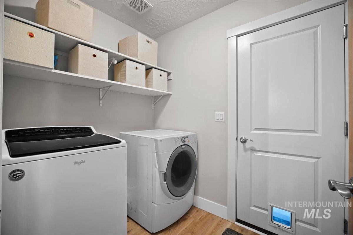 Laundry room featuring light wood finished floors, independent washer and dryer, and a textured ceiling