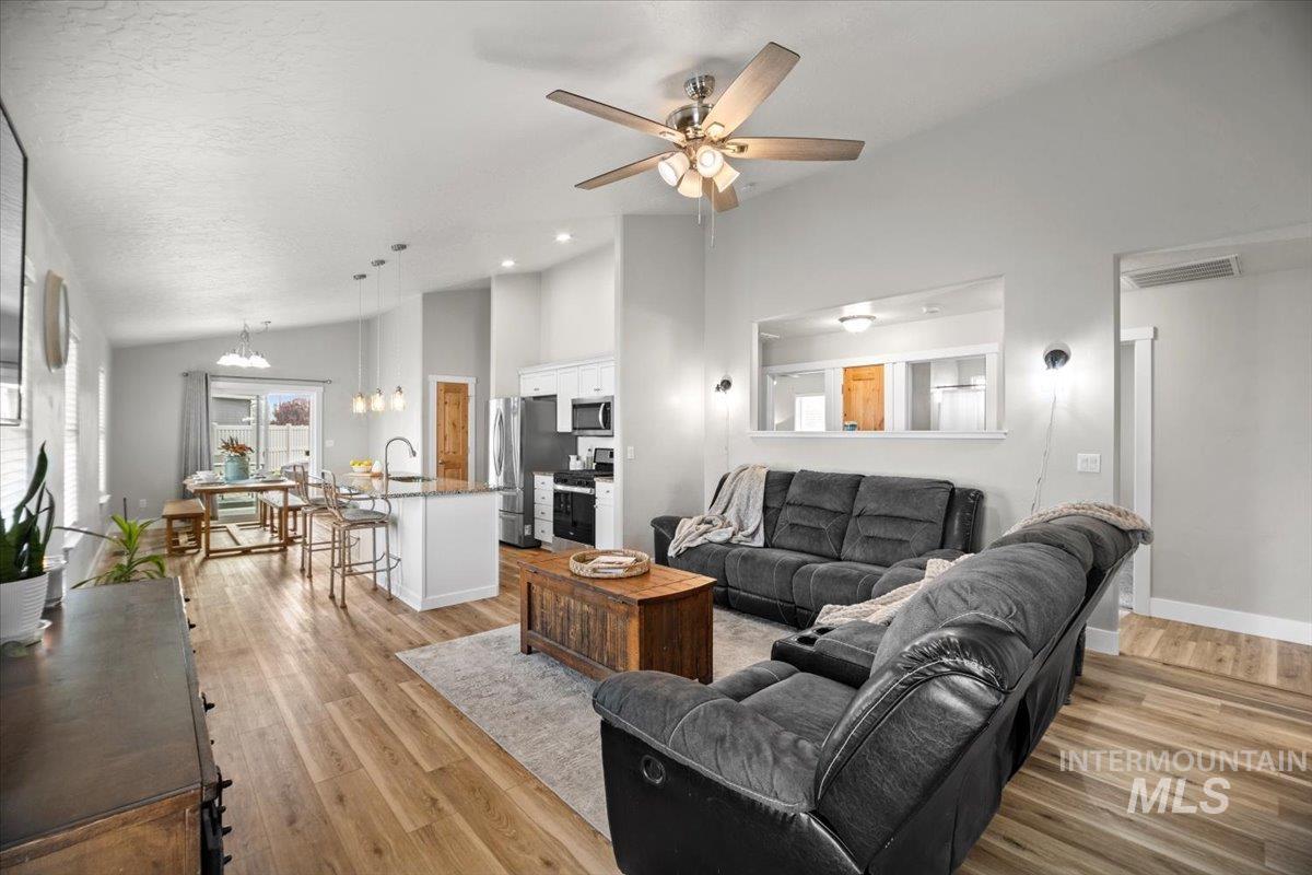 Living area with a chandelier, high vaulted ceiling, light wood finished floors, a ceiling fan, and a textured ceiling