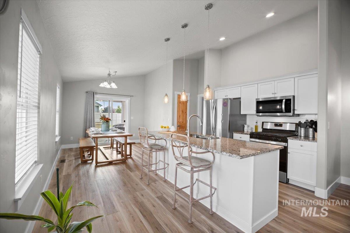 Kitchen featuring stainless steel appliances, a breakfast bar, white cabinets, light stone counters, and light wood-style floors