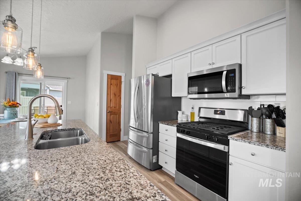Kitchen featuring stainless steel appliances, light stone counters, light wood-style floors, decorative light fixtures, and white cabinetry
