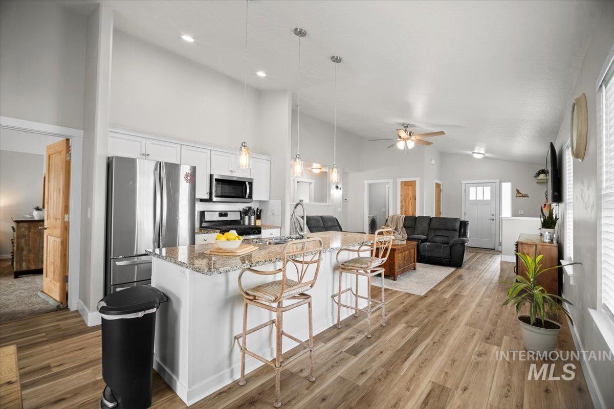 Kitchen with white cabinetry, light stone countertops, hanging light fixtures, stainless steel appliances, and open floor plan