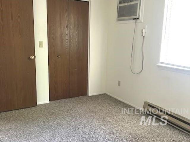 Unfurnished bedroom with a baseboard radiator, two closets, carpet floors, and a wall unit AC