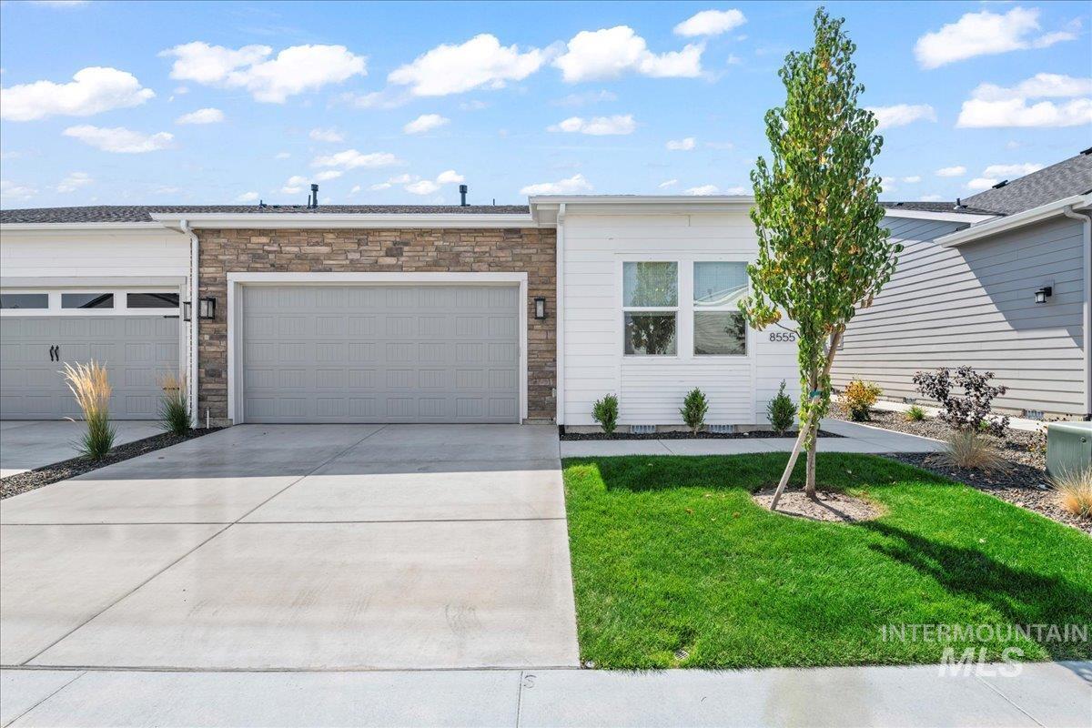 View of front of property with concrete driveway, a garage, stone siding, and a front lawn