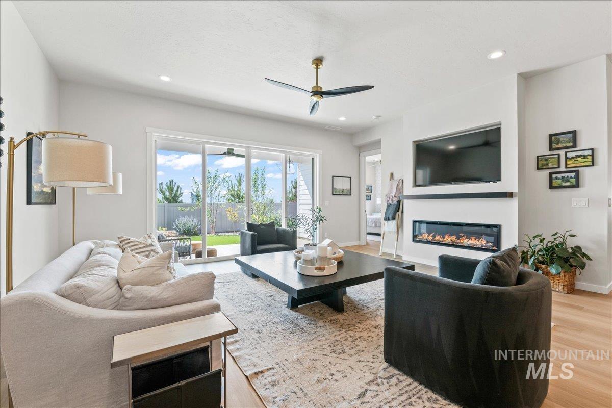 Living area with light wood-style floors, a ceiling fan, recessed lighting, and a glass covered fireplace