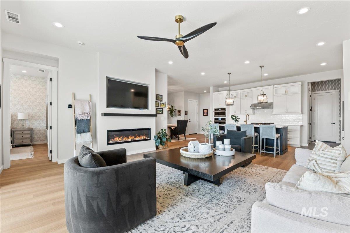 Living area with light wood-type flooring, wallpapered walls, ceiling fan, recessed lighting, and a glass covered fireplace