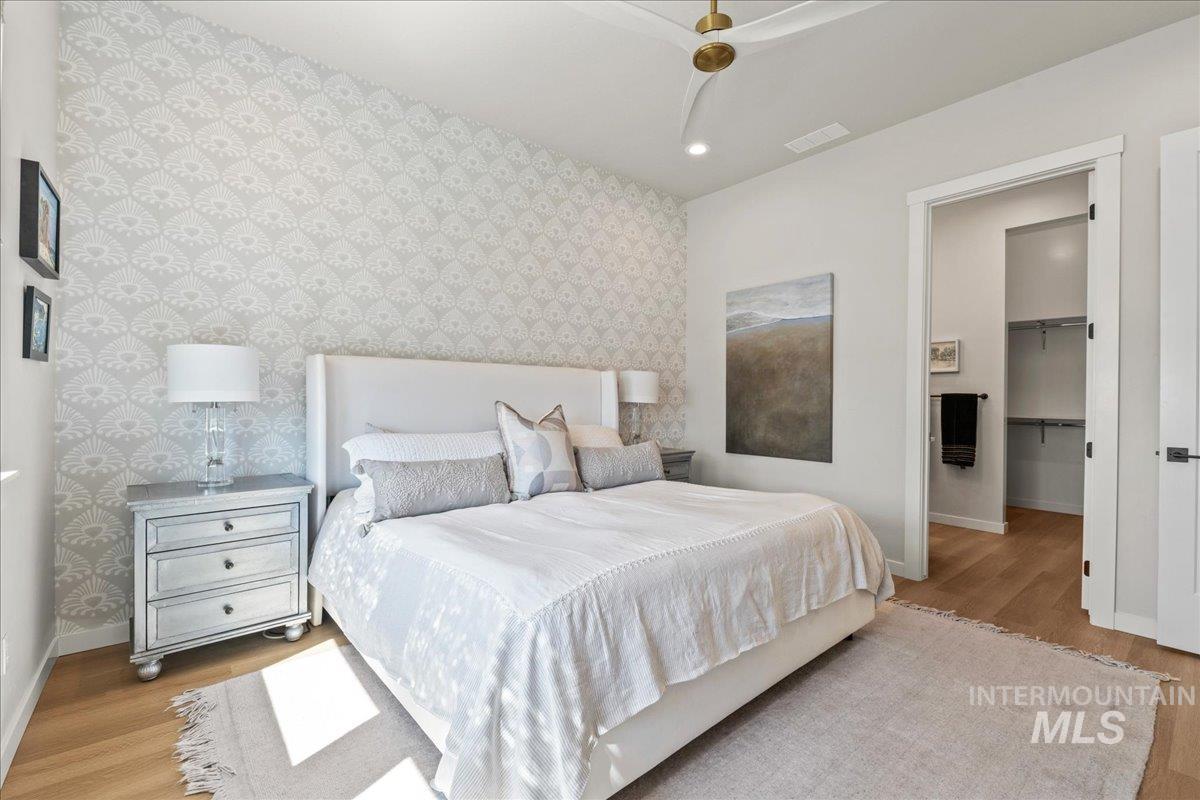 Bedroom featuring wallpapered walls, wood finished floors, a walk in closet, recessed lighting, and an accent wall