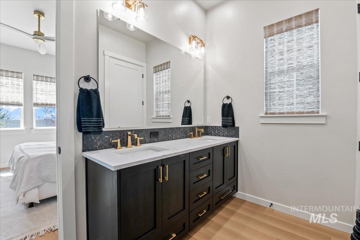 Bathroom with double vanity, light wood-style floors, ensuite bath, and tasteful backsplash