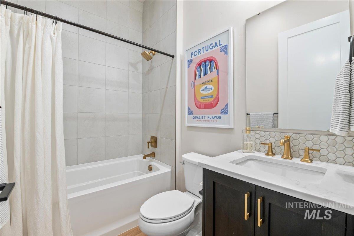 Full bathroom featuring vanity, shower / bathtub combination with curtain, and backsplash