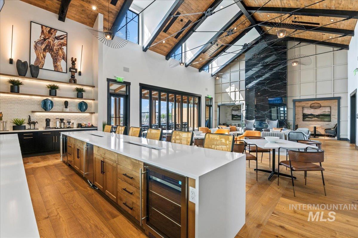 Kitchen featuring beverage cooler, light wood-style floors, high vaulted ceiling, light stone countertops, and brown cabinetry
