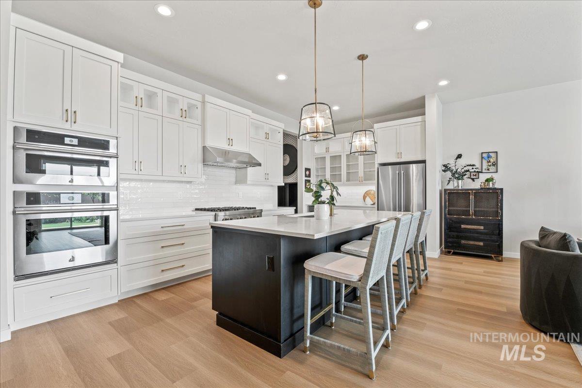 Kitchen with glass insert cabinets, tasteful backsplash, a breakfast bar area, hanging light fixtures, and a kitchen island