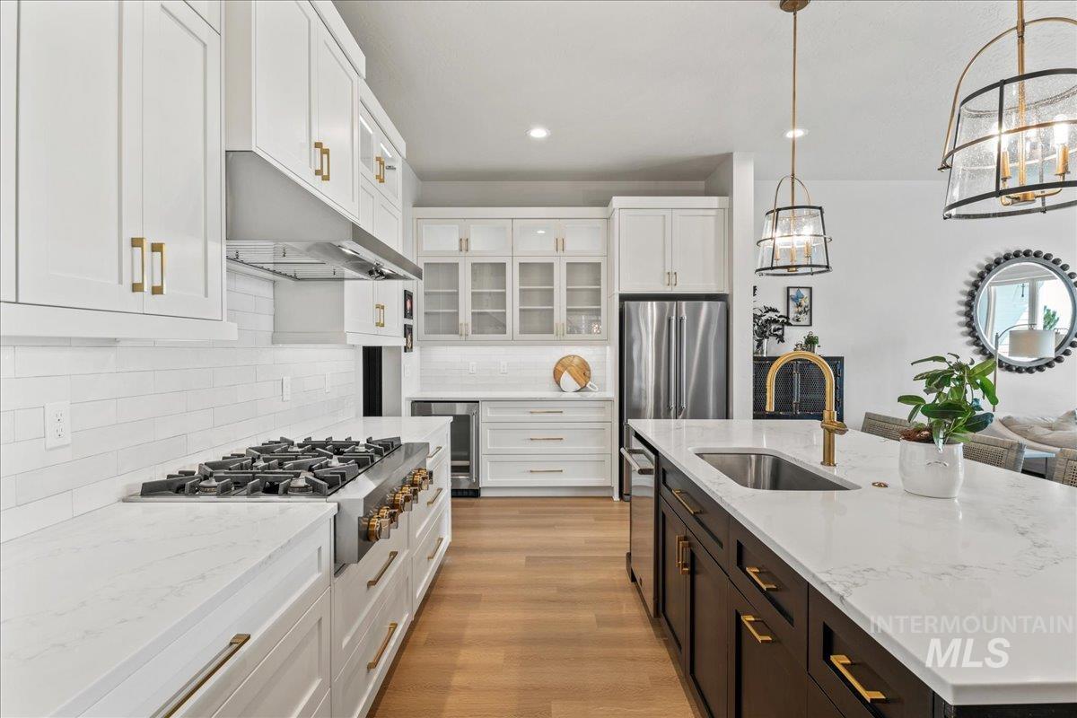 Kitchen with white cabinets, glass insert cabinets, stainless steel appliances, hanging light fixtures, and an island with sink