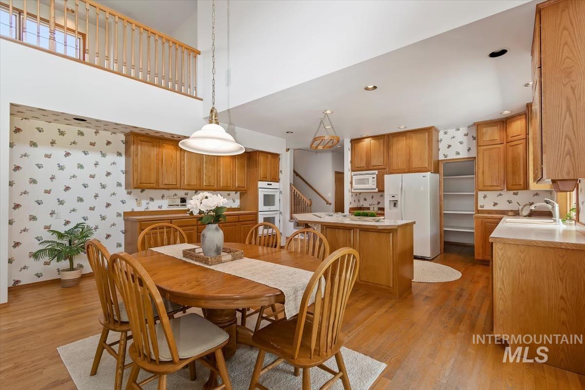 Dining room featuring wallpapered walls, light wood-style floors, stairway, and a towering ceiling
