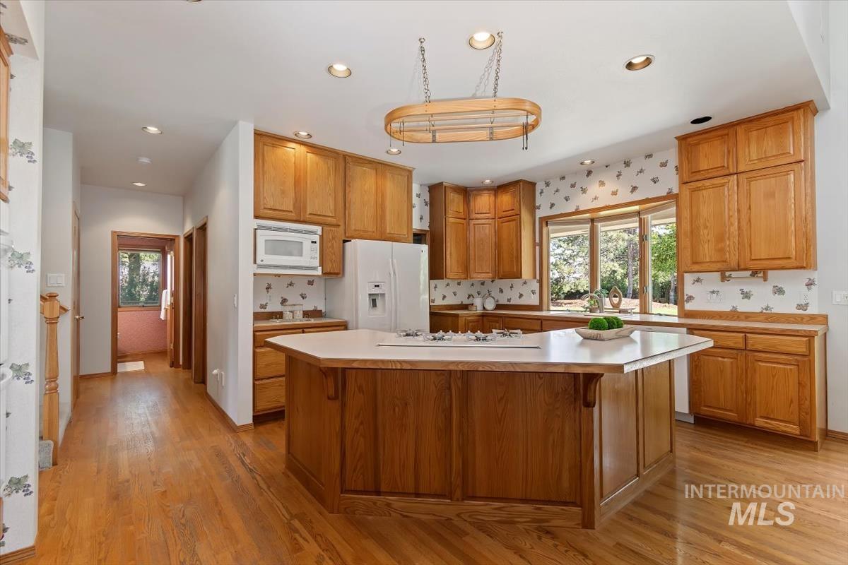 Kitchen with light countertops, light wood-type flooring, white appliances, a center island, and brown cabinets