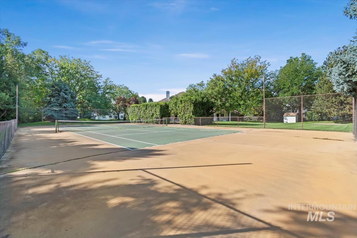 View of tennis court featuring view of wooded area
