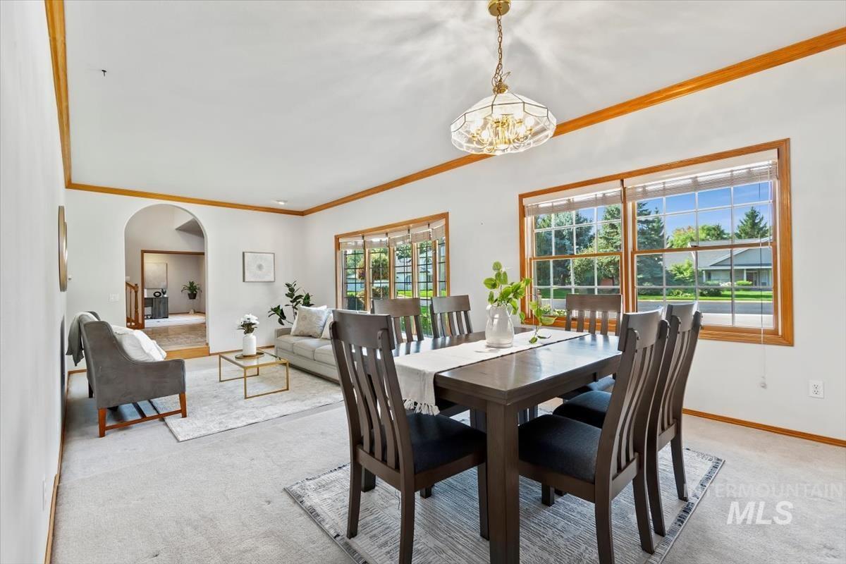 Dining area featuring crown molding, arched walkways, light colored carpet, and a chandelier