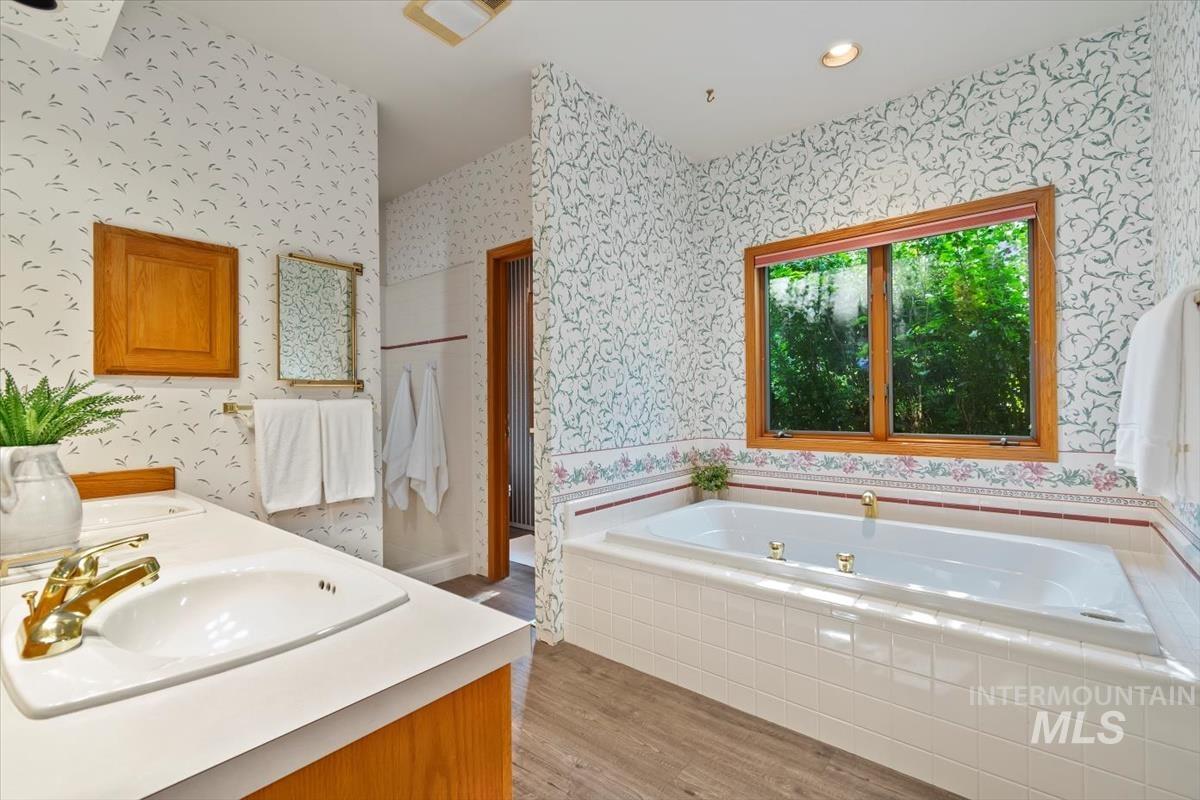 Full bath featuring light wood-style floors, a garden tub, double vanity, wallpapered walls, and recessed lighting