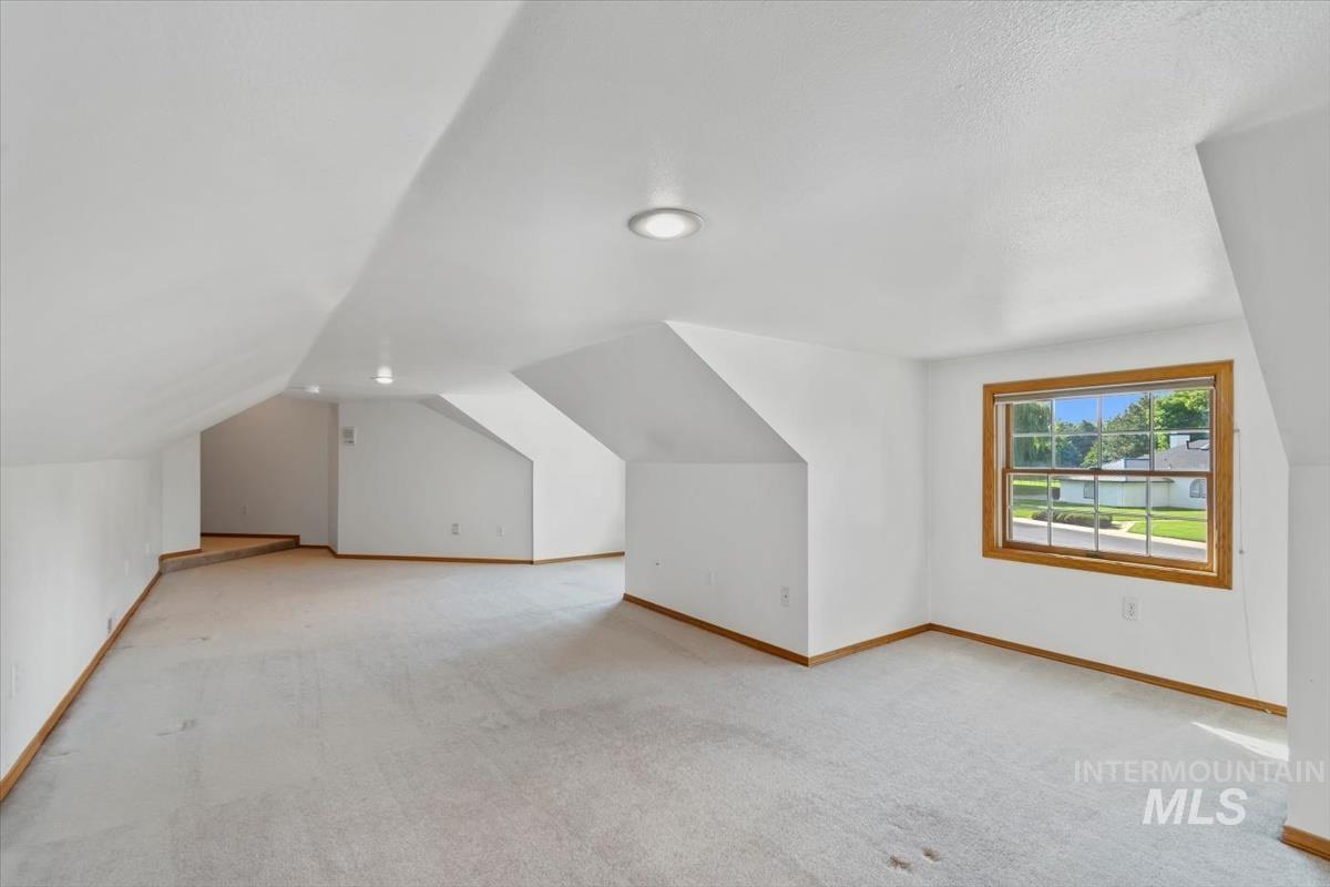 Bonus room with light colored carpet and vaulted ceiling