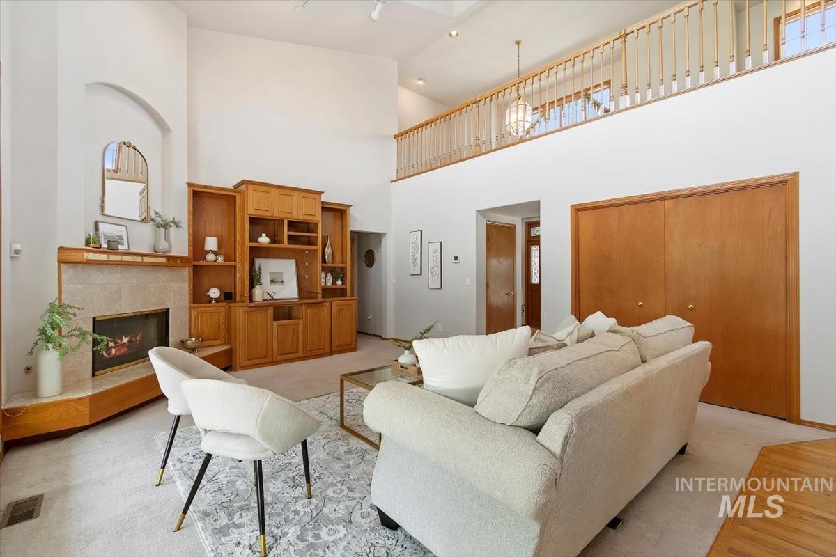 Living room with a tiled fireplace, high vaulted ceiling, and light colored carpet