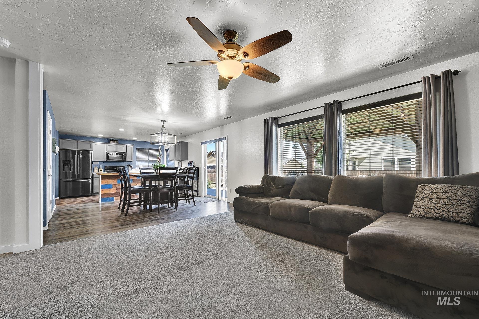Carpeted living room with a textured ceiling, a ceiling fan, and plenty of natural light
