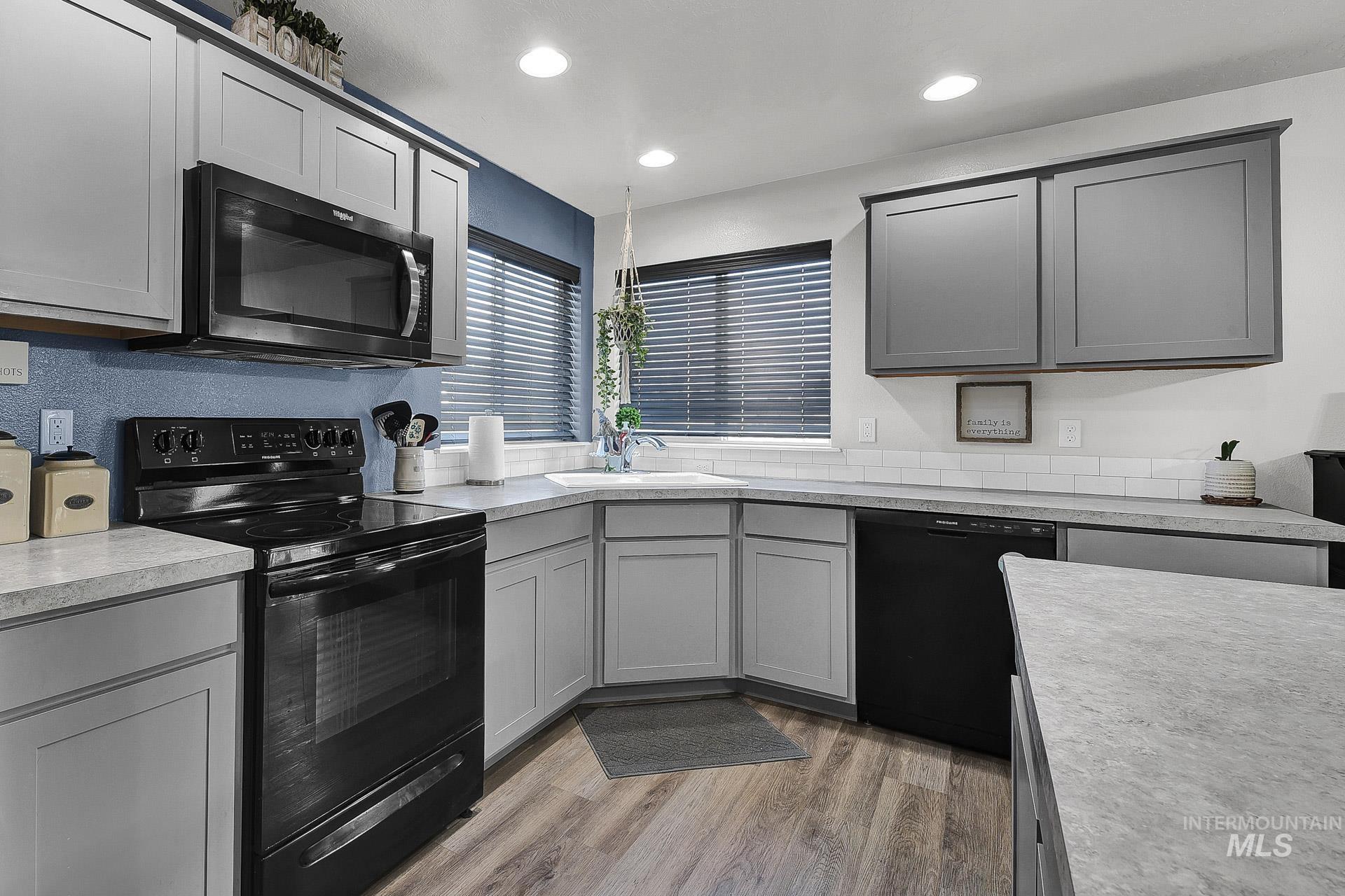 Kitchen with black appliances, gray cabinetry, light wood-type flooring, light countertops, and recessed lighting
