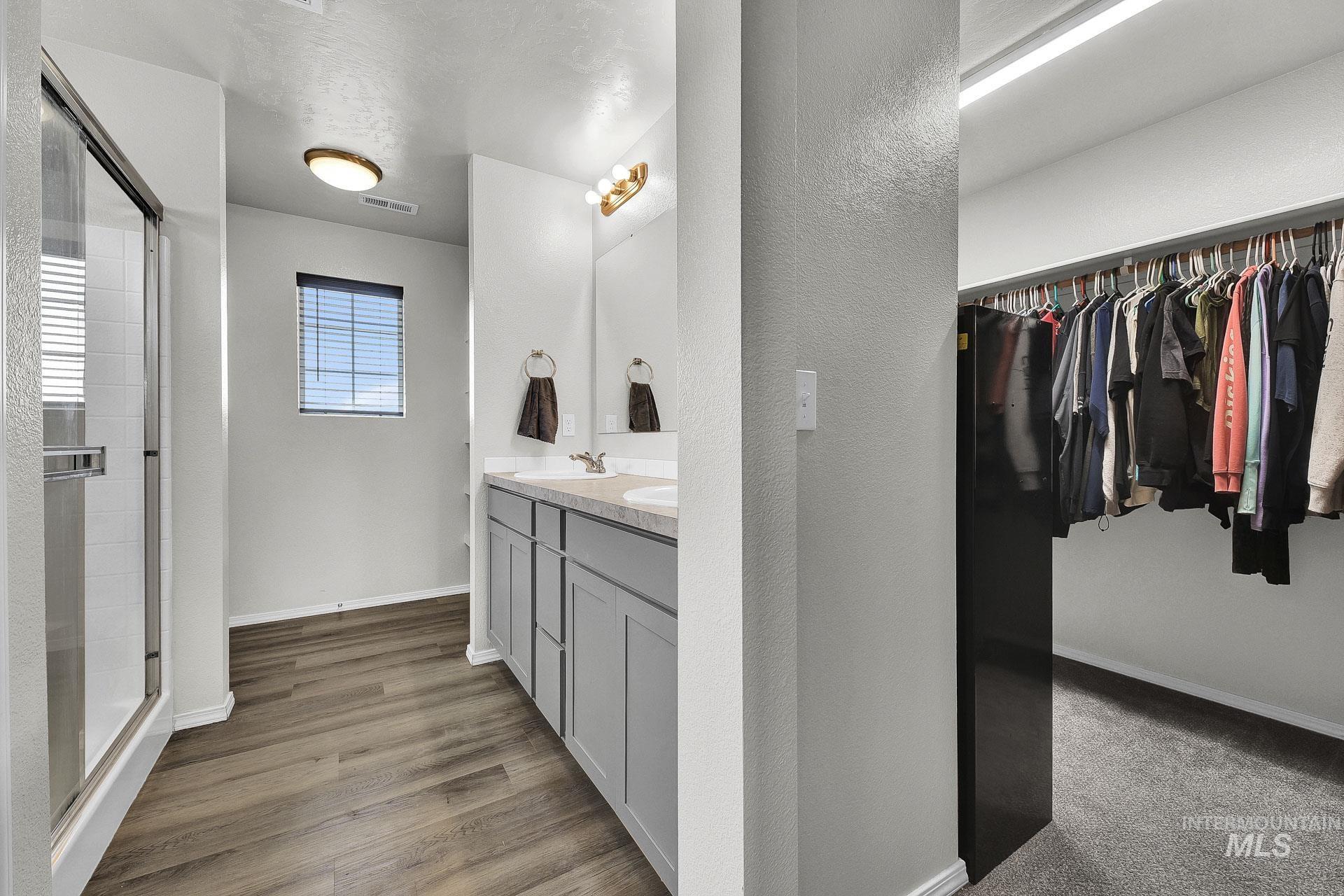 Full bathroom featuring double vanity, a walk in closet, a stall shower, a textured wall, and light wood-style flooring