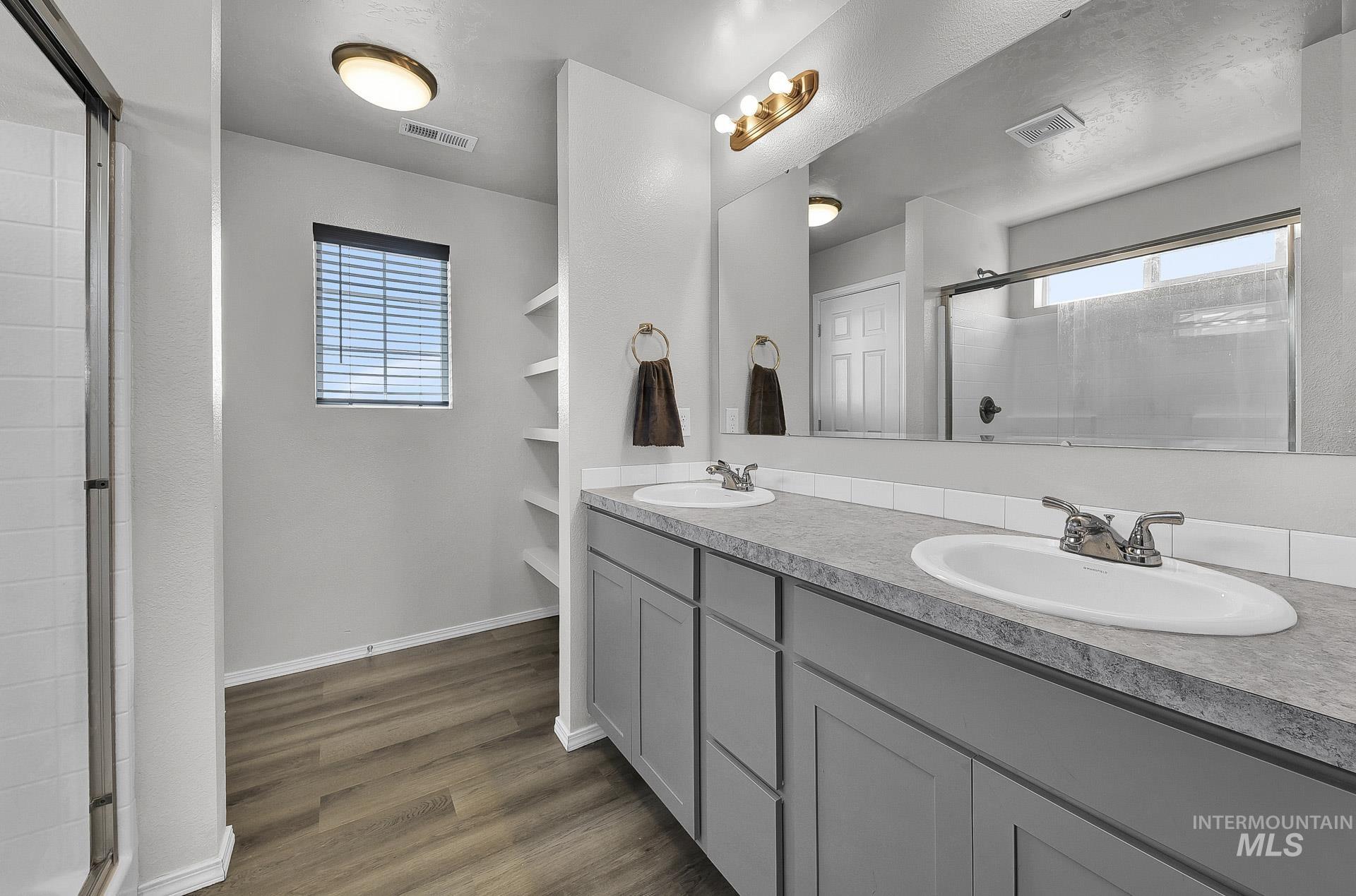 Bathroom featuring a shower stall, double vanity, dark wood-style flooring, and healthy amount of natural light