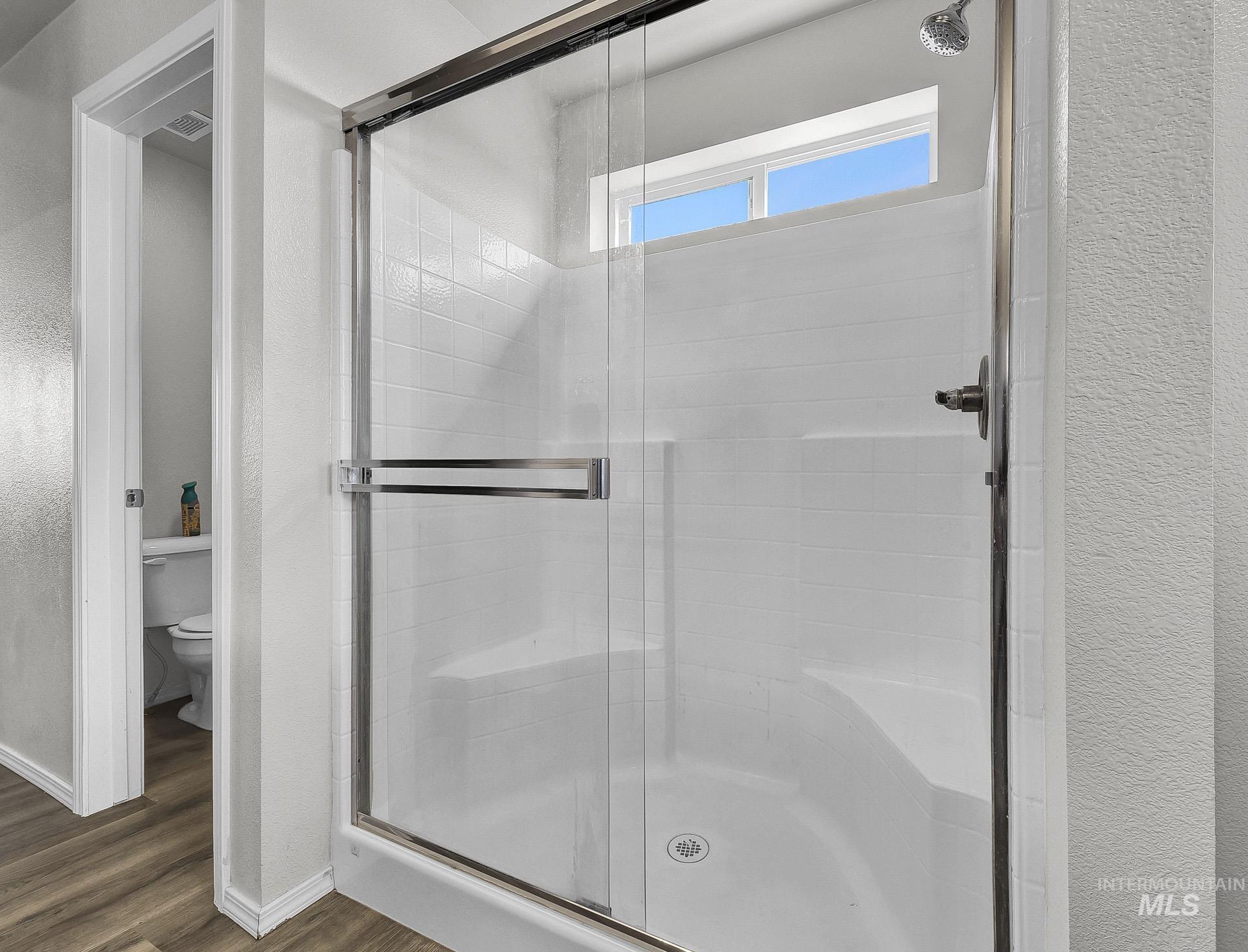 Bathroom with a stall shower, dark wood-style flooring, and a textured wall