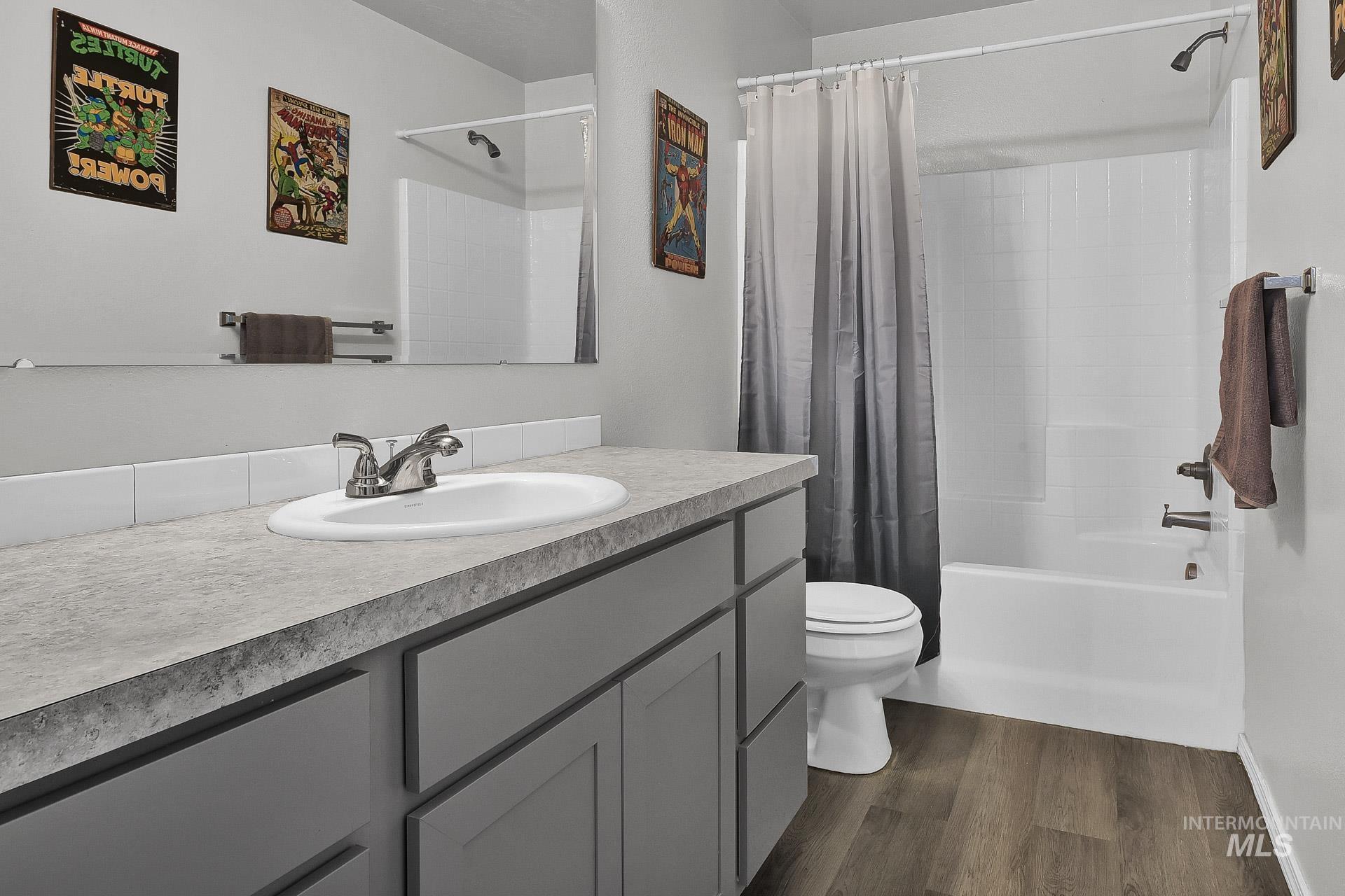 Bathroom with shower / bathtub combination with curtain, vanity, and dark wood-style floors