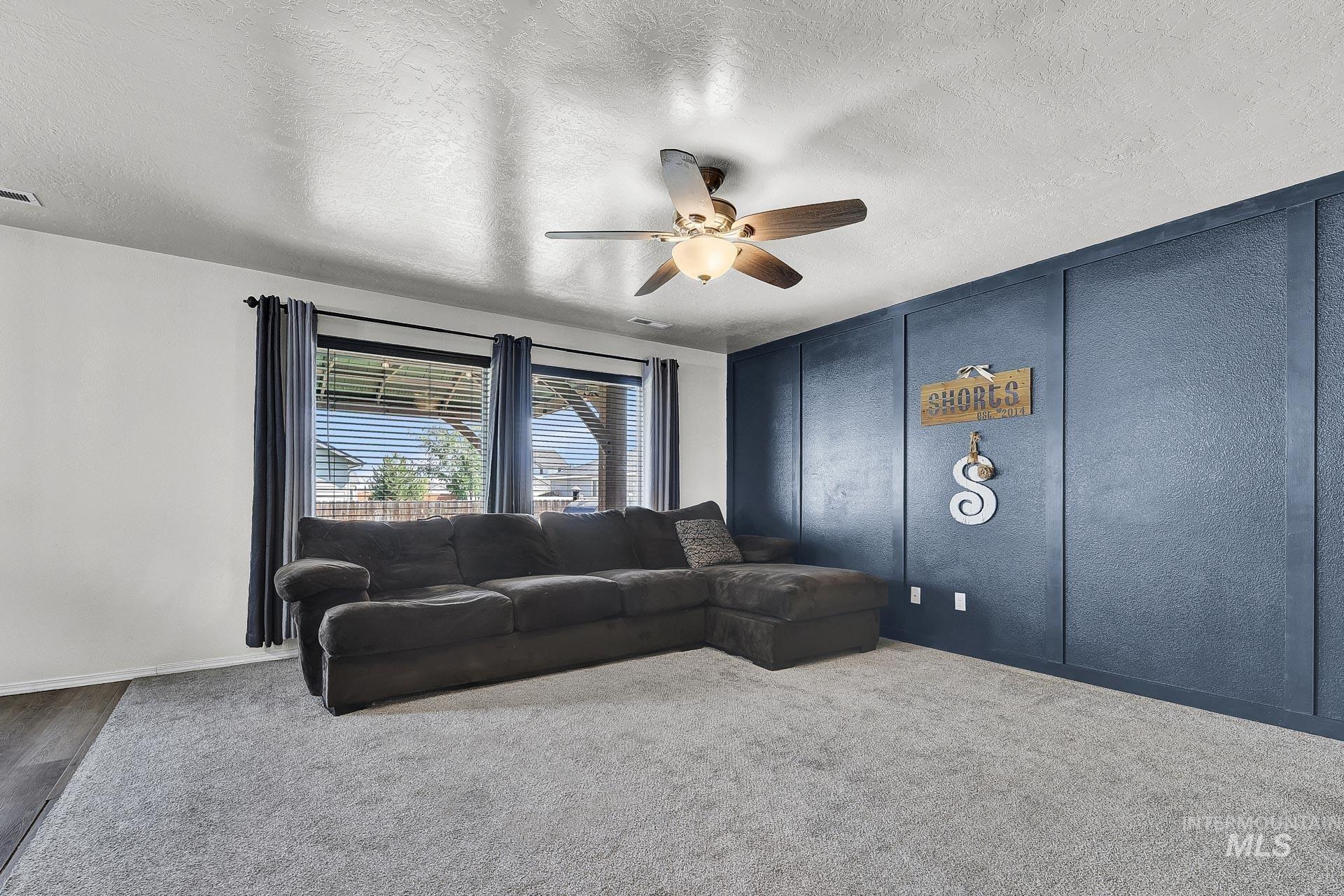 Carpeted living room with a decorative wall, a textured ceiling, and a ceiling fan